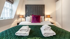 A hotel room with a large bed, two bedside lamps, a window with curtains, and a dark headboard. - Royal Two Bedroom House in Mayfair (London)