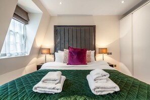 Ein Hotelzimmer mit einem großen Bett, zwei Nachttischlampen, einem mit Vorhängen versehenen Fenster und einem dunklen Kopfteil.