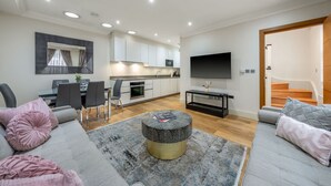 A modern living room with a sofa, ottoman, and a dining area with chairs and a table. - Royal Two Bedroom House in Mayfair (London)