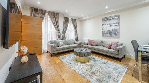 A modern living room with a sofa, coffee table, and a flat-screen TV mounted on the wall. - Royal Two Bedroom House in Mayfair (London)