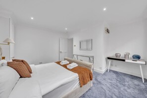 A hotel room with a bed, a desk, a mirror, and a door. - Superior 3 Bedroom Apartment in Belgravia w Patio (London)