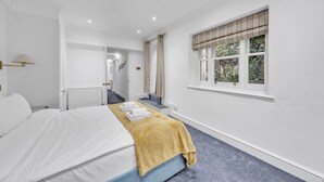 Una camera d'albergo con un letto, una finestra con tende, un termosifone e una scala che conduce a un'altra stanza.