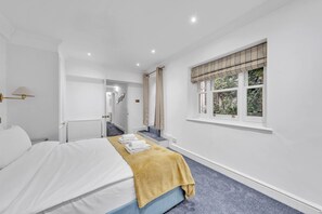 A hotel room with a bed, a window with curtains, a radiator, and a staircase leading to another room. - Superior 3 Bedroom Apartment in Belgravia w Patio (London)