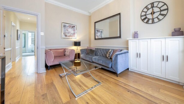 A living room with a sofa, a glass coffee table, a cabinet, a clock, and a mirror on the wall. - Exclusive 2-bedroom Apartment (London)