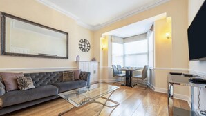 A living room with a sofa, glass coffee table, and a dining area with chairs and a table. - Exclusive 2-bedroom Apartment (London)