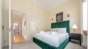 A bedroom with a green upholstered headboard, a white bedspread, and a bedside lamp. - Exclusive 2-bedroom Apartment (London)