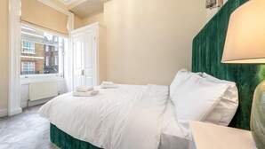 A hotel room with a bed, a window, a radiator, and a green wall. - Exclusive 2-bedroom Apartment (London)