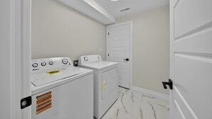 A laundry room with a washer and dryer, a white door, and a ceiling light. - The Windsor Mainstay (Windsor)