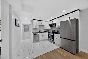 A modern kitchen with white cabinets, stainless steel appliances, and a marble floor.