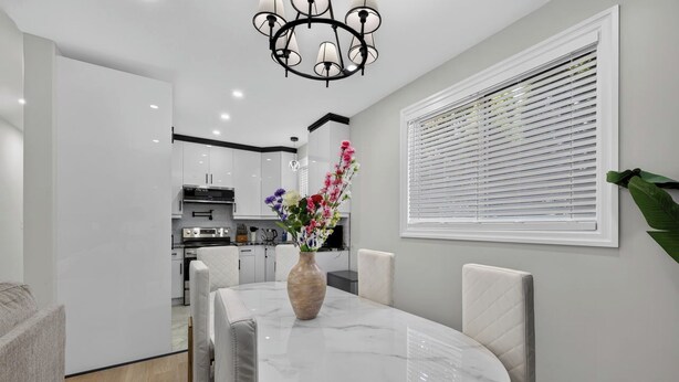 A modern dining area with a marble table, white chairs, and a vase of flowers. - The Windsor Mainstay (Windsor)