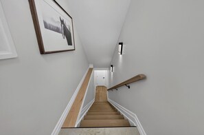 A staircase with wooden steps, white walls, and a framed picture on the left.