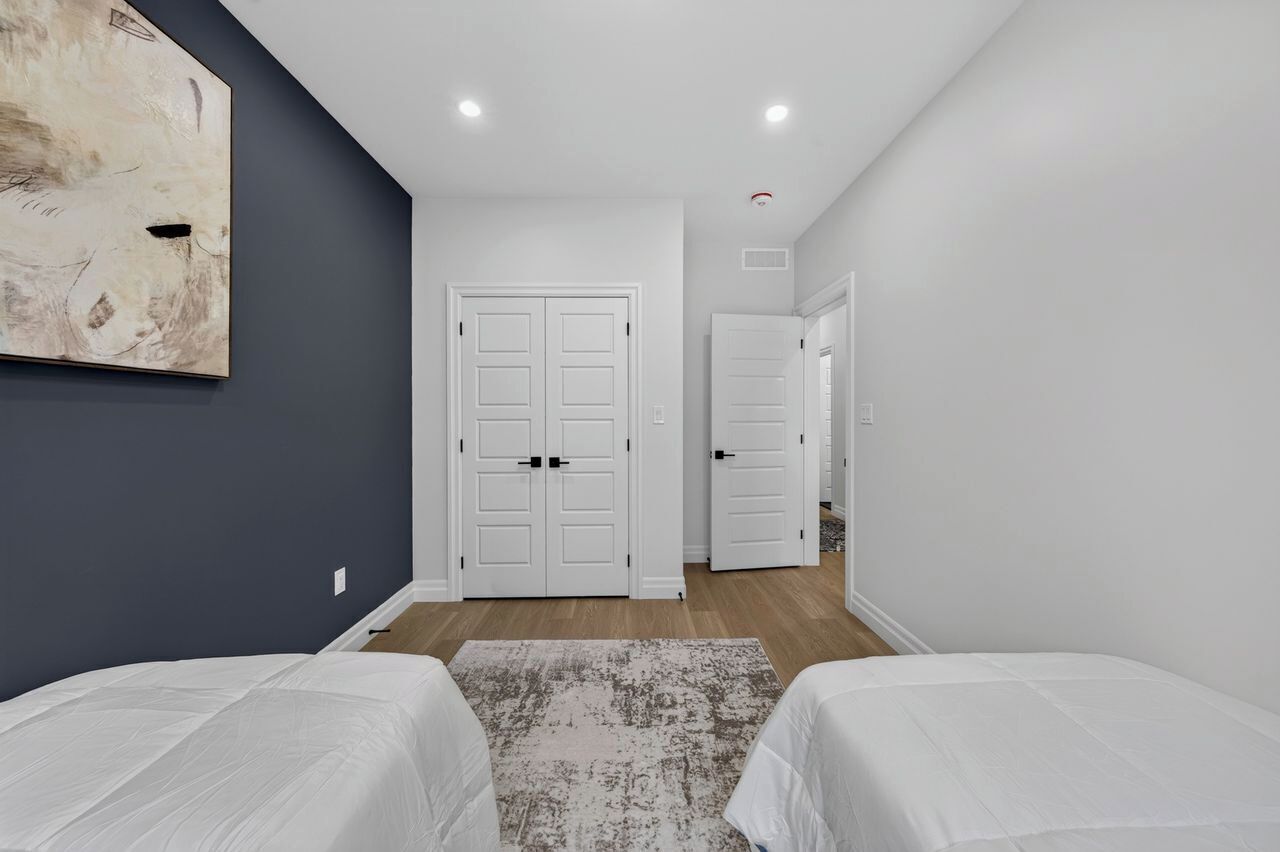 A bedroom with two beds, a large abstract painting, and a hallway leading to another room.