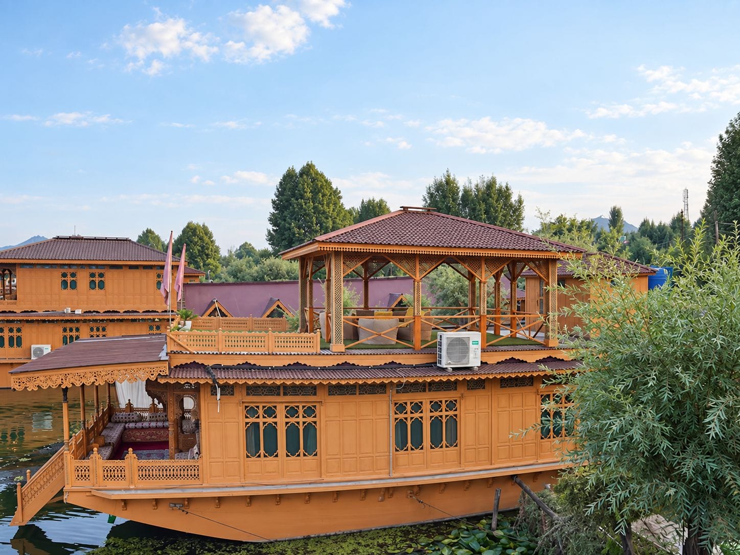 Uma casa-barco de madeira tradicional com um deck coberto, um pequeno pavilhão e um corpo de água ao fundo.