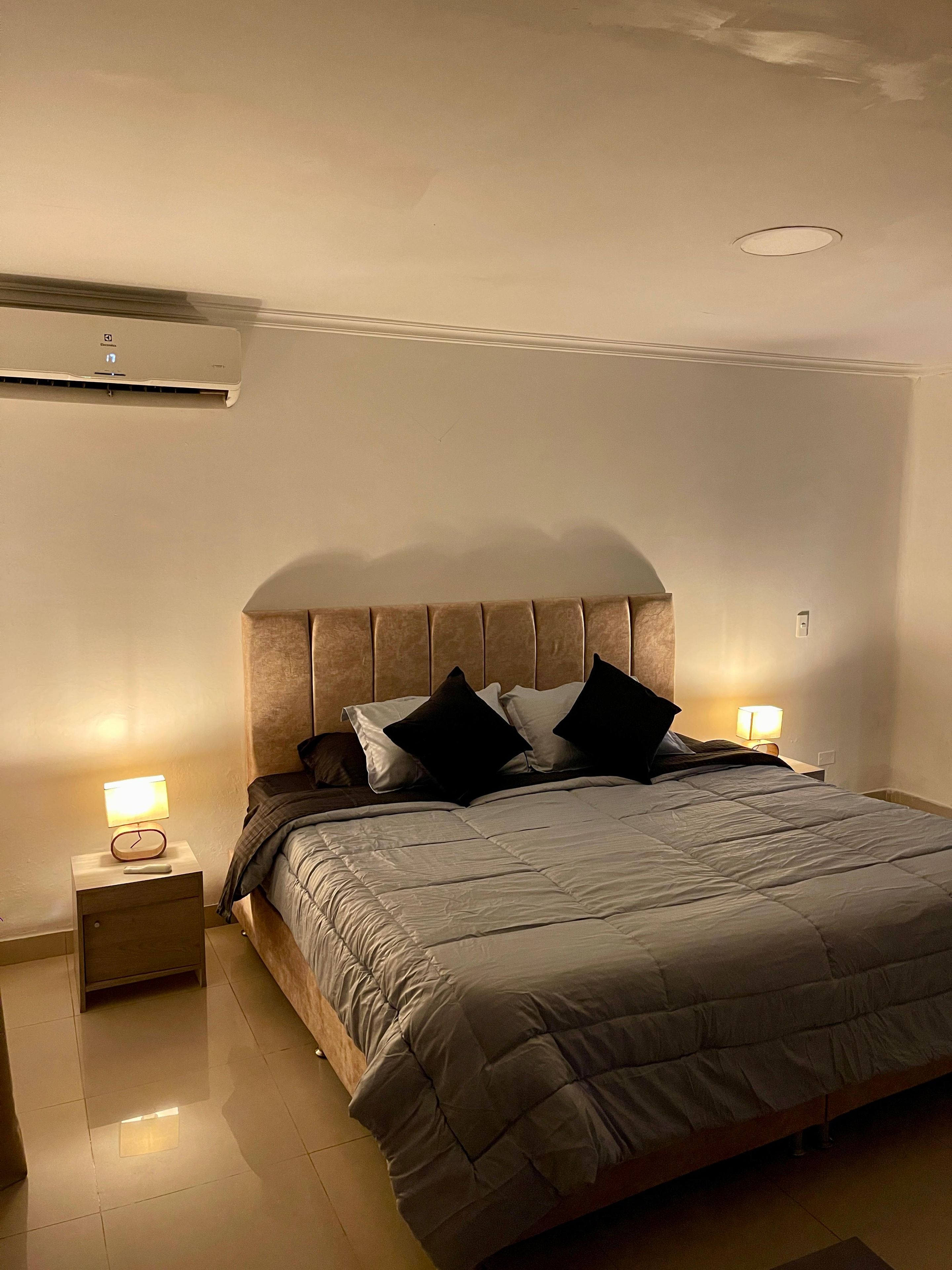 A bedroom with a bed, nightstands, a wall-mounted air conditioner, and a ceiling light fixture.