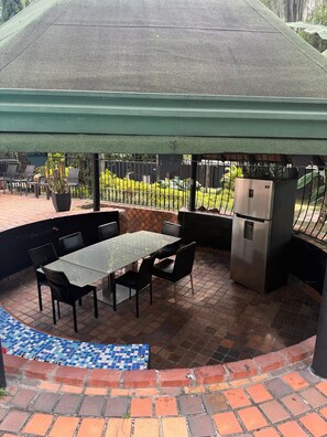 Eine Terrasse im Freien mit einem Tisch und Stühlen mit Glasplatte, einem Kühlschrank und einem Blumentopf.