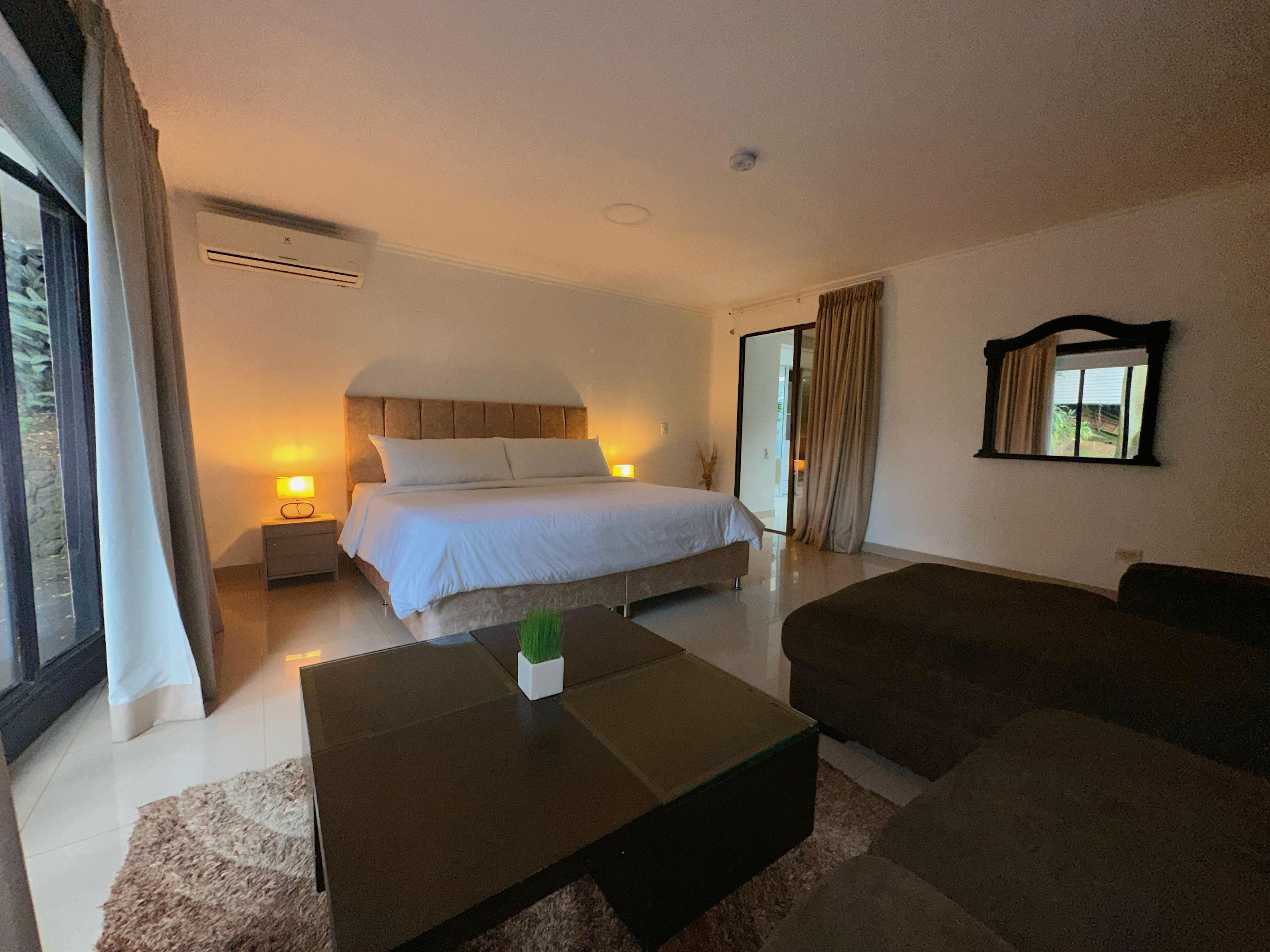 Un dormitorio con cama, mesitas de noche, una mesa de centro y una ventana con cortinas.