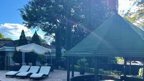 Un área de piscina con sillones de descanso, una zona de estar cubierta y un borde de piscina con azulejos.