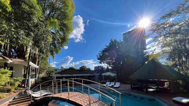 Una piscina con un puente, sillas de descanso y un pabellón.