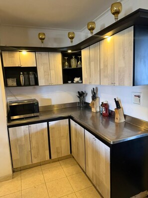 A kitchen with wooden cabinets, a stainless steel countertop, and a microwave.