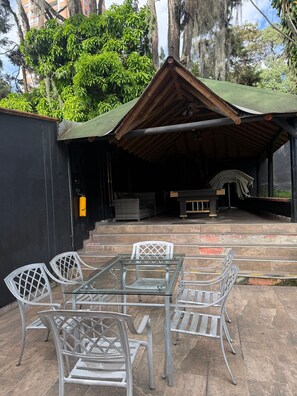 An outdoor seating area with a table and chairs, a covered patio, and a view of trees and buildings in the background. - Private Poblado Tropical Estate 10BR Pool 18Person Jacuzzi Walk to GoldenMile AC (Medellín)