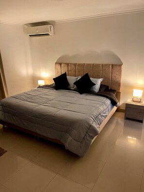 A hotel room with a bed, nightstands, and an air conditioning unit.