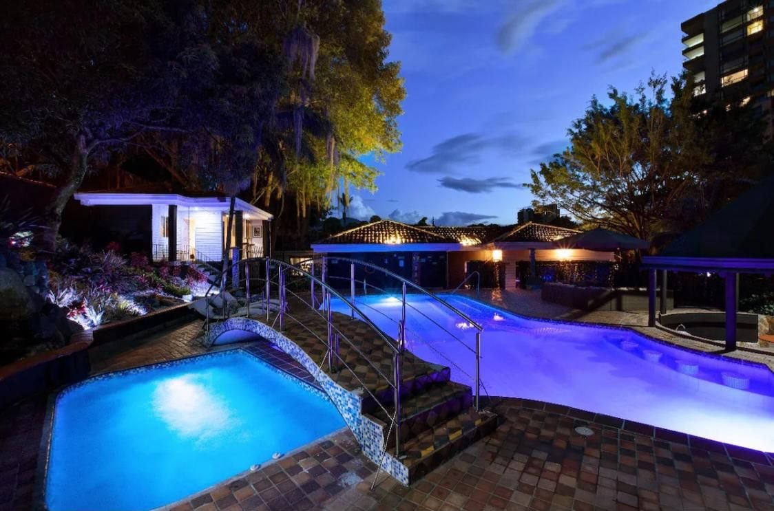 Un área de piscina nocturna con una terraza cubierta y un edificio contiguo.