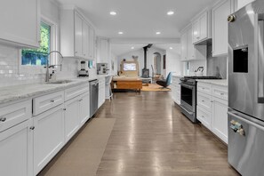 A modern kitchen with white cabinets, stainless steel appliances, and a wooden floor. - Stylish home in Historic Forest Park perfect for a family retreat (Birmingham)