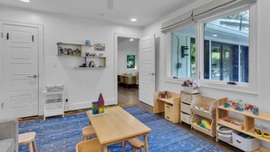 Ein Zimmer mit Holztisch, Stühlen, einem Bücherregal und einem Fenster mit Jalousien.