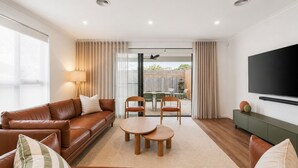 A living room with a sofa, two chairs, a coffee table, a TV, and a sliding glass door leading to an outdoor area. - The Cowes Retreat by Ready Set Stay (Cowes)