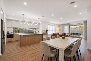 Eine moderne Küche mit Kochinsel, Essbereich mit Tisch und Stühlen sowie ein Wohnbereich mit Sofa und Vorhängen.
