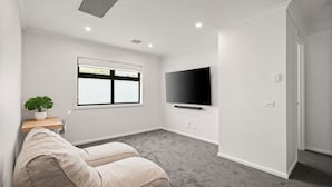 A modern living room with a flat-screen TV, a potted plant, a beige sofa, and a window with blinds. - The Cowes Retreat by Ready Set Stay (Cowes)