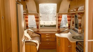 Een compact RV-interieur met een kitchenette, een bed en een raam met gordijnen.
