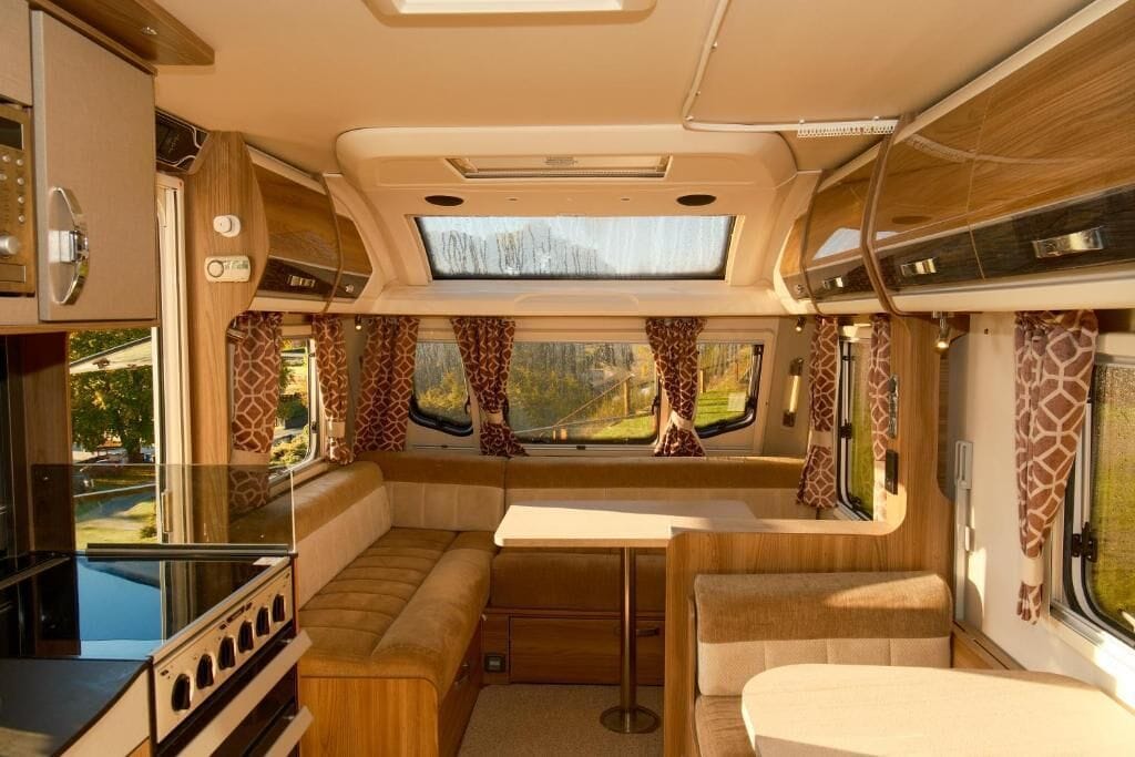 A well-lit RV interior with a kitchen, dining area, and seating.