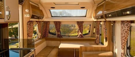 A well-lit RV interior with a kitchen, dining area, and seating.