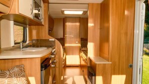 A compact kitchen with a sink, stove, and cabinets, and a door leading to a sleeping area. - Sundale Caravan Retreat 4 Berth - Wanaka (Wānaka)