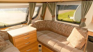 A compact RV interior with a kitchenette, a cushioned seating area, and windows with curtains. - Sundale Caravan Retreat 4 Berth - Wanaka (Wānaka)