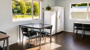 A modern kitchen with a dining table, chairs, a refrigerator, and a window with a view of a park. - Sundale Caravan Retreat 4 Berth - Wanaka (Wānaka)