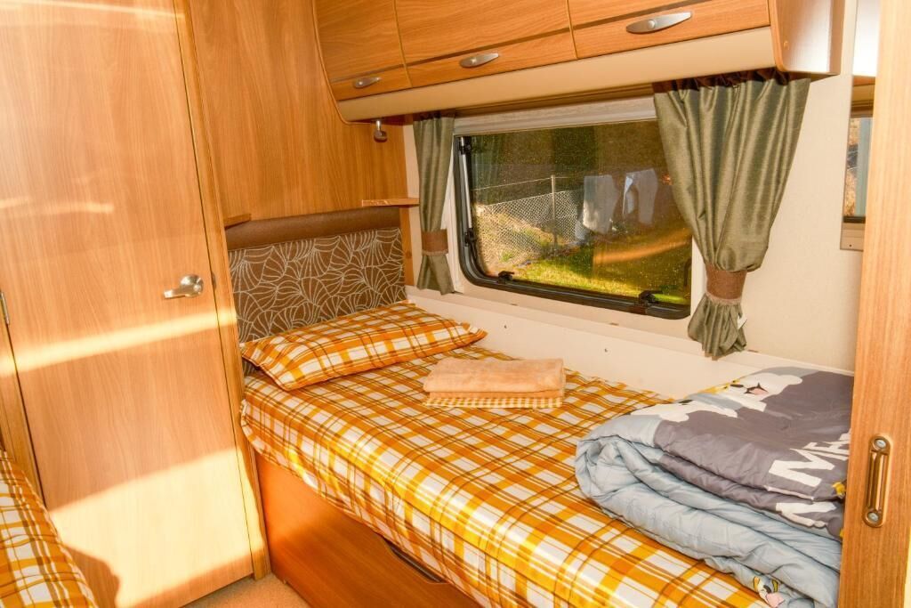 Een ruimtelijk camperinterieur met een bed, een raam met gordijnen en houten kastjes.