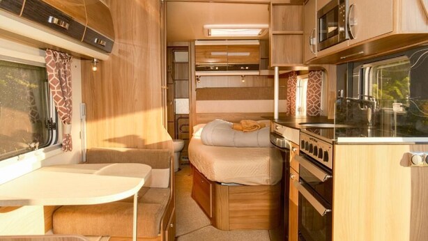 A compact RV interior with a kitchenette, a bed, and a dining area. - Sundale Caravan Retreat 4 Berth - Wanaka (Wānaka)