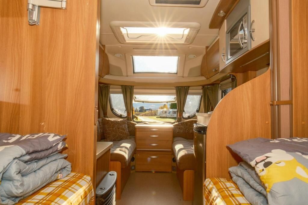 A compact RV interior with two beds, a kitchenette, and a sunroof.