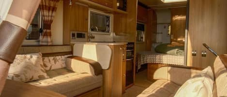 A compact RV interior with a kitchenette, a dining area, and a sleeping space.