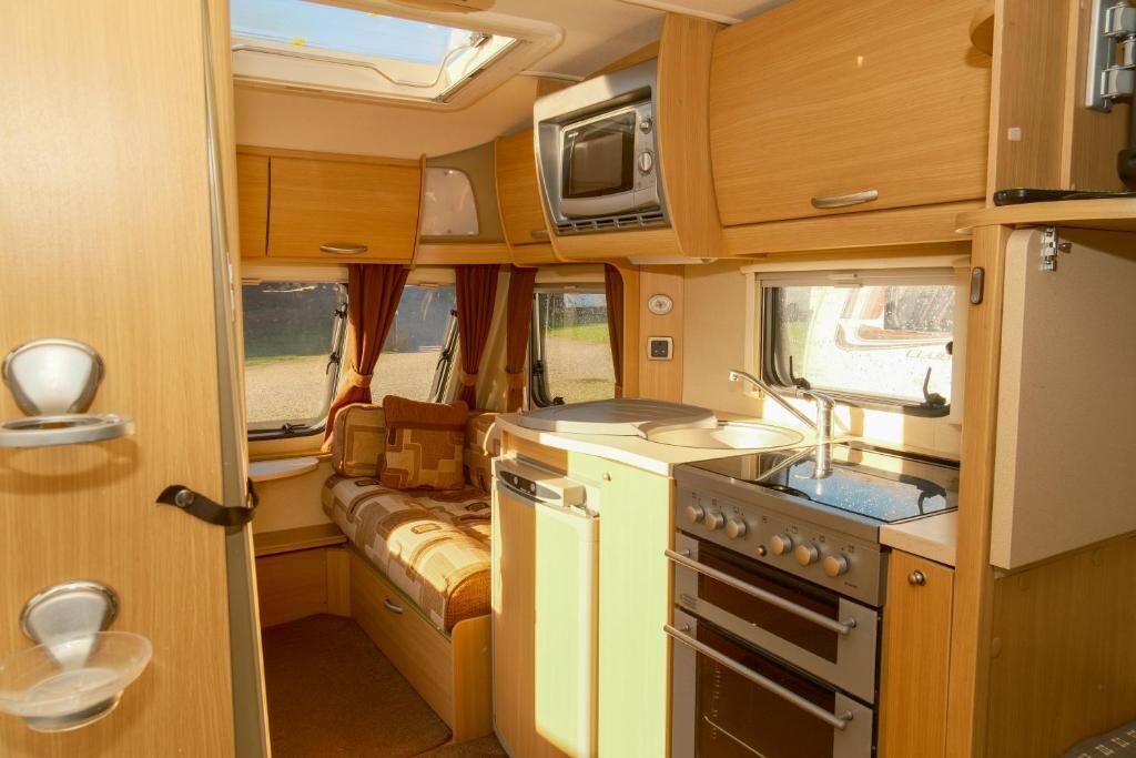 Interior compacto de RV com cozinha compacta, uma cama e uma pequena área de refeições.