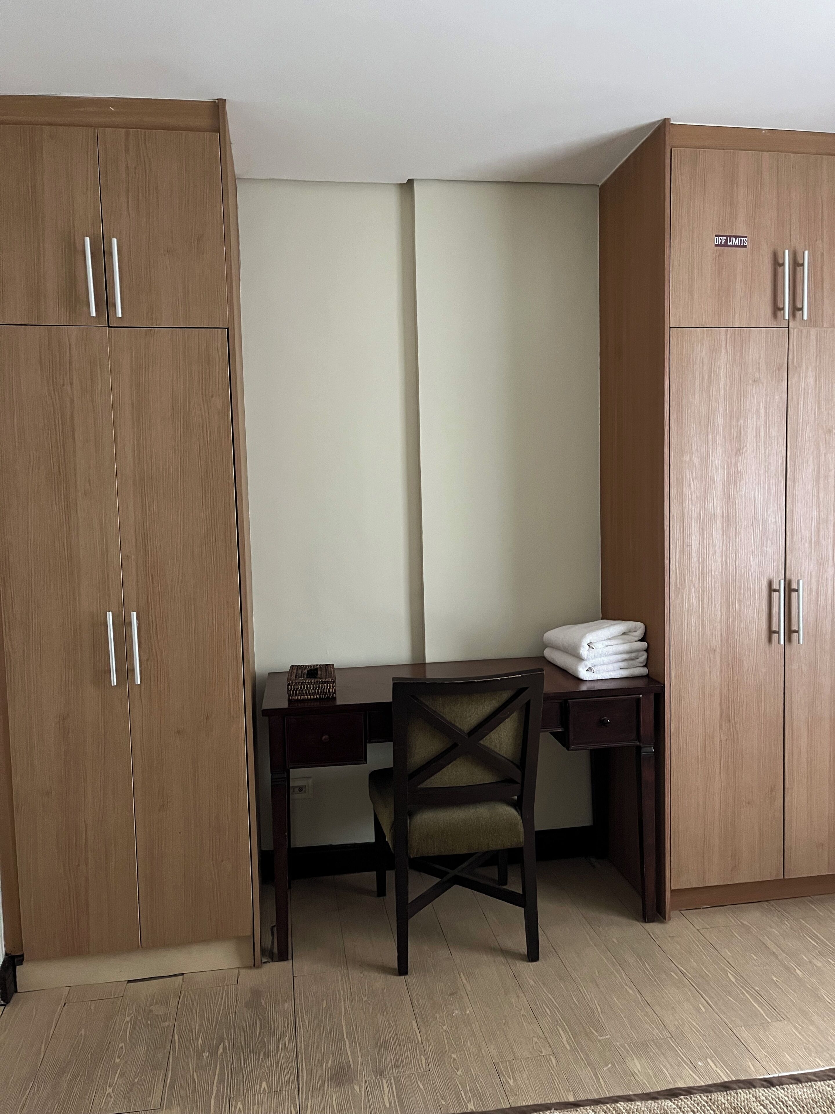 Una habitación con un armario de madera, un escritorio con una silla y una toalla doblada sobre el escritorio.