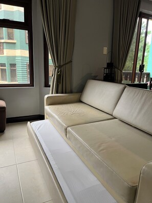 A room with a sofa, a window with curtains, and a view of buildings outside. - One Bedroom Mountain Respite at Crosswinds (Tagaytay City)