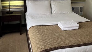 Hotellihuoneessa on sänky, yöpöytä, lamppu ja kaksi kehystettyä kuvaa seinällä.