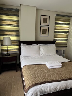 A hotel room with a bed, a nightstand, a lamp, and two framed pictures on the wall. - One Bedroom Mountain Respite at Crosswinds (Tagaytay City)