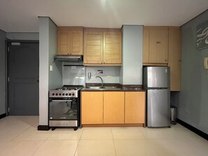 A compact kitchen with wooden cabinets, a stainless steel stove, a sink, and a refrigerator. - One Bedroom Mountain Respite at Crosswinds (Tagaytay City)
