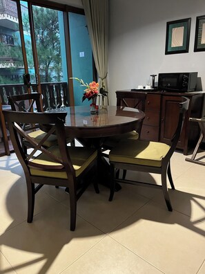 A dining area with a round table, chairs, a vase with flowers, a cabinet, and a microwave. - One Bedroom Mountain Respite at Crosswinds (Tagaytay City)