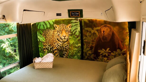 Et lille værelse med en seng, et lille bord, en lampe og et vægmaleri af en jungle.