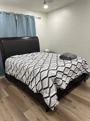 A bedroom with a bed, a nightstand, a towel, and a window with curtains.